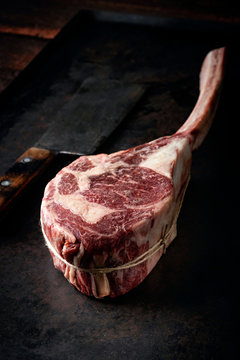 Raw Tomahawk steak dry aged with a meat cleaver on a dark stone background