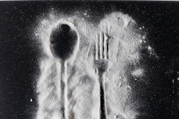 White sugar on black background with silhouette of spoon and fork