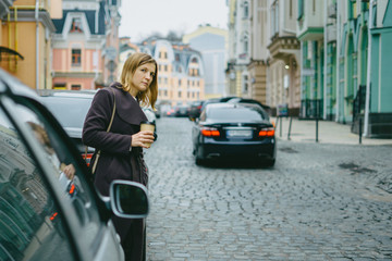 Stylish young woman crossing city streets with cup of coffee