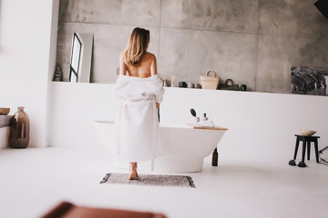 Beautiful woman relaxing in white bathrobe near bath - obrazy, fototapety, plakaty