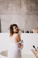 Beautiful woman relaxing in white bathrobe near bath