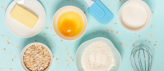 Ingredients for baking oat cookies on a blue background, top view, flat lay. Flour, butter, egg, oatmeal and sugar in bowls on the table
