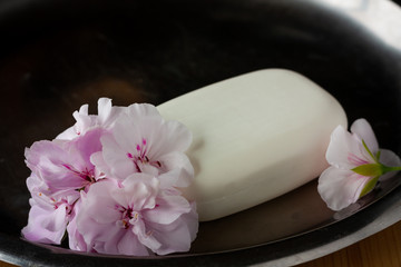 Obraz na płótnie Canvas White soap with soft geranium pink flowers and white towel on a steel tray for hygiene and spa