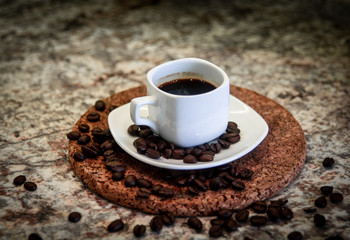 A small cup of espresso and coffee beans on a stand