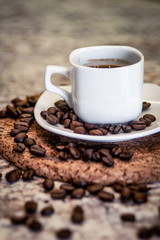 A small cup of espresso and coffee beans on a stand