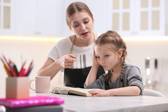 Woman helping her daughter with homework at table in kitchen