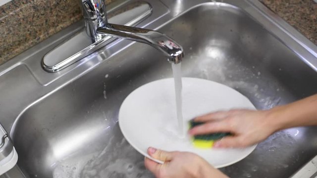 Woman washing dishes in the kitchen sink. Female hands rinse plate at the sink