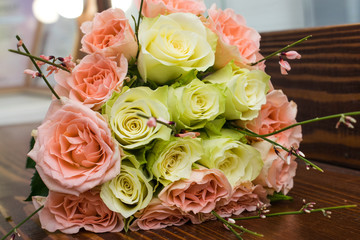 Elegant wedding bouquet of white and pink roses and genista lying on the brown wooden table