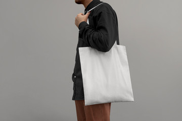 Urban mockup of tote bag. Men holding black cotton tote bag on a wall background. Template can be...