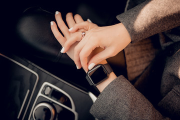 Photo of female hands touching setting of digital smart watch in car.