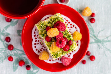 Spinach cream cake with cranberry and raspberry berries on a red plate, top view