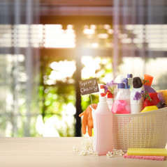 Plastic basket with different detergents on wooden table indoors, space for text. Spring cleaning concept