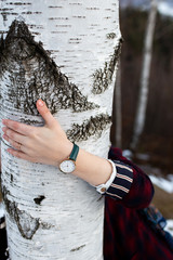 Close up photo of female hand wearing  green watch. She is holding her hand on beautiful white birch tree.