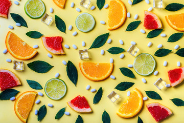 Pattern of citrus lemon, lime, orange and grapefruit slices, mint herbs, cubes of ice and fresh pills on yellow background. Top view. Minimal design background.