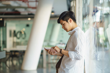 Smiling asian business man standing, using mobile phone.  © Songsak C