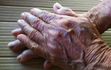 The hand of an old woman, on a brown background, intimate care is at her home, focus at close range of elderly portraits.