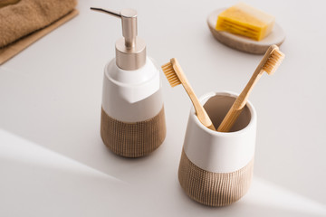 Fototapeta na wymiar Close up view of liquid soap, toothbrush holder with toothbrushes, towels and dish with soap on grey, zero waste concept