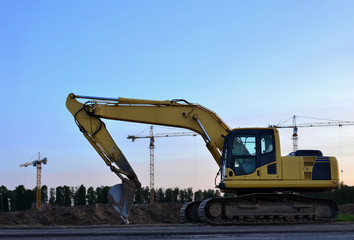 Excavator at a construction site on sunset background. Road repair, asphalt replacement. Digging the ground for the foundation and construction of a new build. Small sharpness, possible granularity