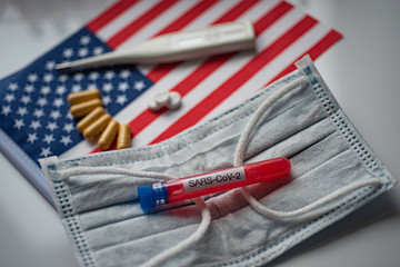 Capsules, pills and thermometer on flag of USA background. Blood test SARS-CoV-2 tube on medical mask. Coronavirus treatment concept.