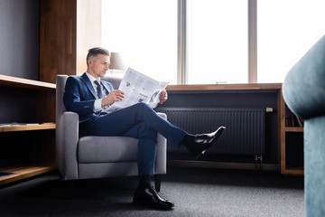 businessman in suit sitting in armchair and reading newspaper in hotel