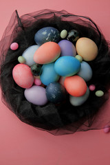 Multicolored eggs and lollipops in a nest of black fabric on a pink background, Easter.