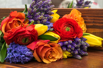 Bright spring bouquet of yellow tulips,blue hyacinths,speedwell,red ranunculus and orange roses lying on the brown wooden table.Present concept for Birthday, mother's Day, 8 March.Selective focus