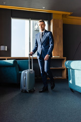 handsome businessman in suit walking with travel bag in hotel