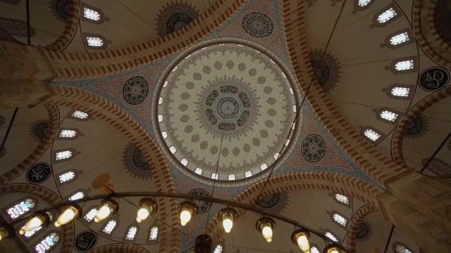 Embroidered ceiling image of the domed mosque and slow motion view of the large chandelier hanging from the ceiling.