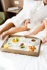 Obraz na płótnie Canvas cropped view of boyfriend and girlfriend in bathrobes sitting near tray with food