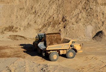 Wheel loader loads sand into heavy mining dump truck at the opencast mining quarry. Heavy machinery in the open pit, excavators, dozers and trucks. Digging and excavation operations
