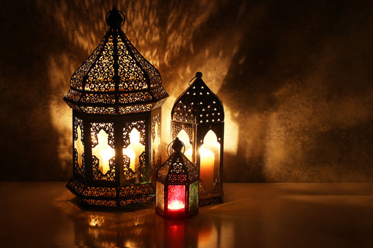 Ornamental Arabic Lanterns With Burning Candles On Table Glowing At Night. Festive Greeting Card, Invitation For Muslim Holy Month Ramadan Kareem. Iftar Dinner Background With Golden Glow.