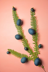 Painted eggs under a stone, lying on a pink background in the leaves of a fern, Easter.