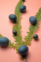 Painted blue eggs lying on a pastel pink background in fern leaves, Easter.