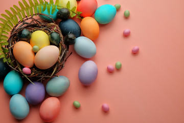 Multicolored eggs and lollipops in a nest on a pink background with a sprig of fern, Easter.