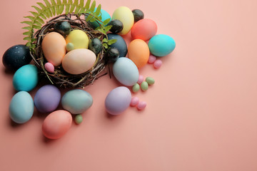 Multicolored eggs and lollipops in a nest on a pink background with a sprig of fern, Easter.