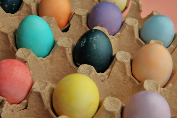 Many colored eggs lie in cardboard trays on a pink background in a checkerboard pattern.
