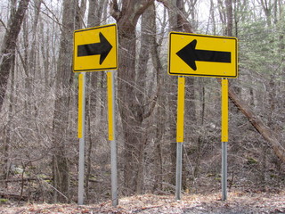Two yellow direction arrow signs pointing towards each other 