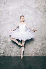 Elegant ballerina in white dress dancing against rustic wall