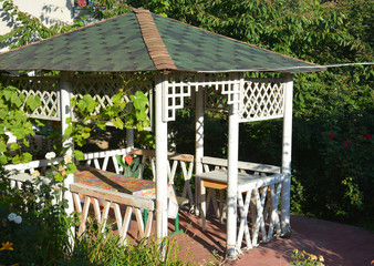 Cozy white wooden gazebo or pergola design. Vinyl garden octagonal gazebo in the corner of a yard.