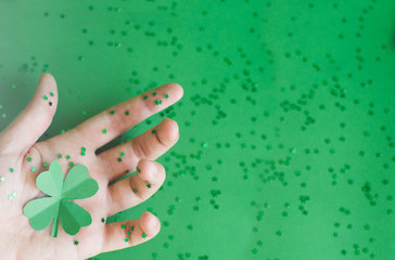Top view of green four-leafed paper clovers on womans hand sprinkled with small stars on green blurred background