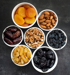 Dried fruits in white bowls on a dark background to maintain cardiovascular health top view