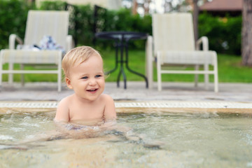 Happy little caucasian blond toddler boy swimming in wading pool on bright summer day at resort....