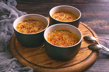 Homemade creme brulee - traditional french vanilla cream dessert with caramelised brown sugar on top, wooden plate and table. Top view, flat lay with copy space.