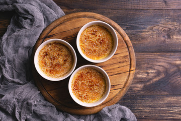 Homemade creme brulee - traditional french vanilla cream dessert with caramelised brown sugar on top, wooden plate and table. Top view, flat lay with copy space.