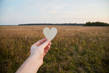 Eco housing and environmentally friendly lifestyle of home owners. Hand holding heart shaped sign on field background
