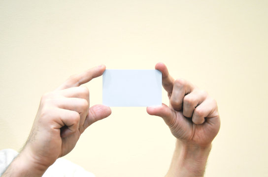 Business card in hands is clean and white. Credit, discount or bank card, customer card is not held in hand on a yellow background.