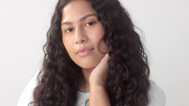 Mixed race plus size woman without makeup in studio watching to the camera and touch her face