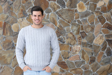 Happy man in warm sweater near stone wall. Space for text