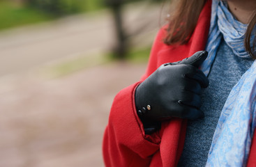 A young girl holds the collar of her coat with a stylish black leather glove.