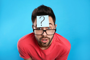 Fototapeta premium Emotional young man with question mark sticker on forehead against light blue background
